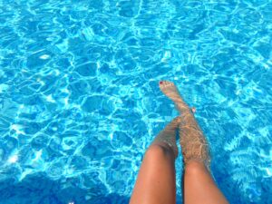Frau kühlt ihre Füße im Pool ab.